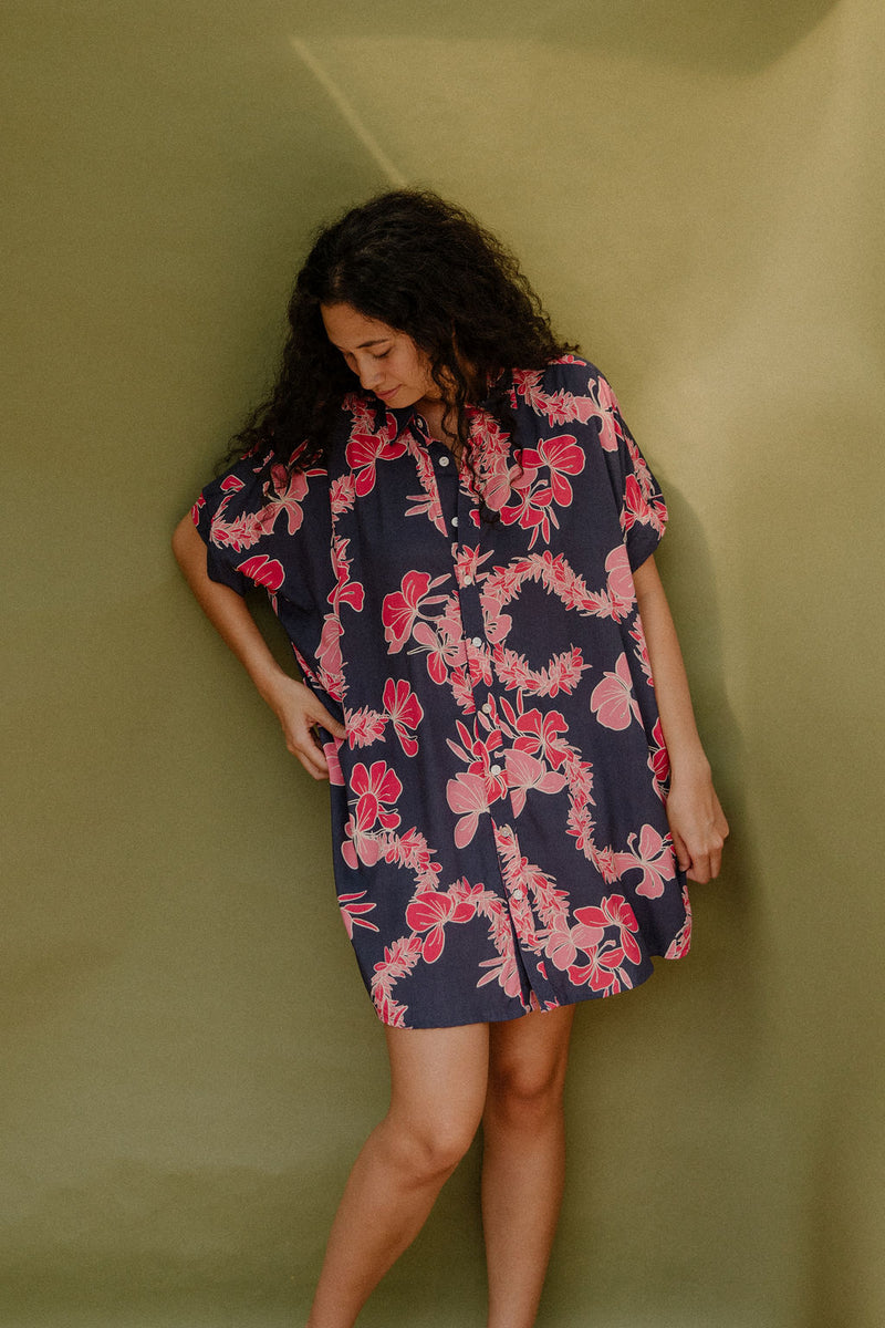 Woman wearing short sleeve shirt dress with pink floral print on dark navy ground.