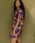 Woman wearing short sleeve shirt dress with pink floral print on dark navy ground.