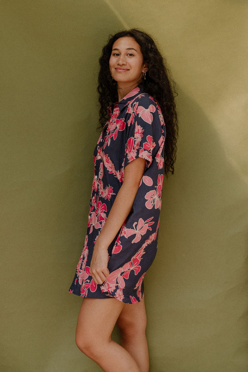 Woman wearing short sleeve shirt dress with pink floral print on dark navy ground.