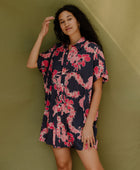 Woman wearing short sleeve shirt dress with pink floral print on dark navy ground.