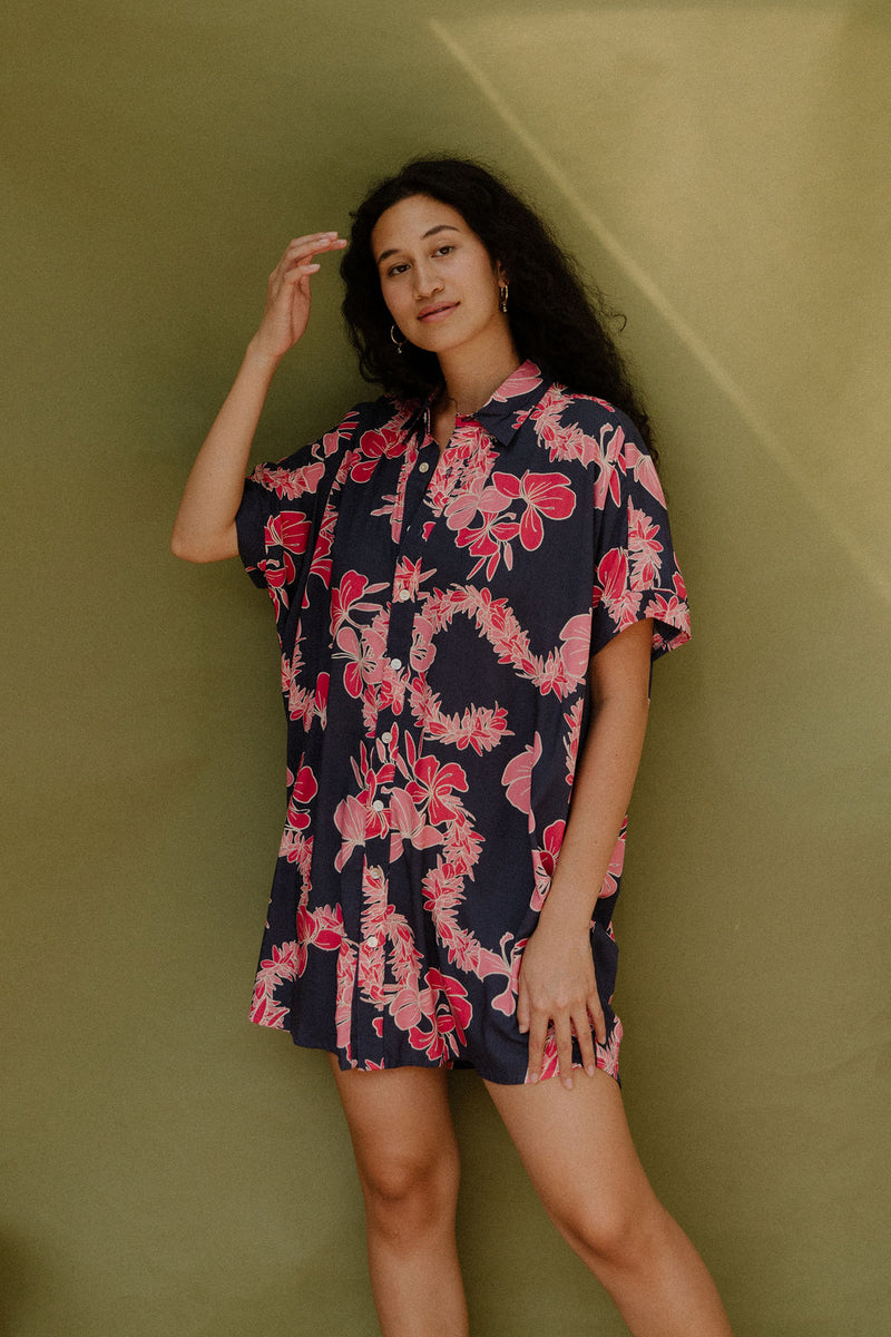 Woman wearing short sleeve shirt dress with pink floral print on dark navy ground.