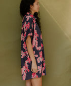 Woman wearing short sleeve shirt dress with pink floral print on dark navy ground.