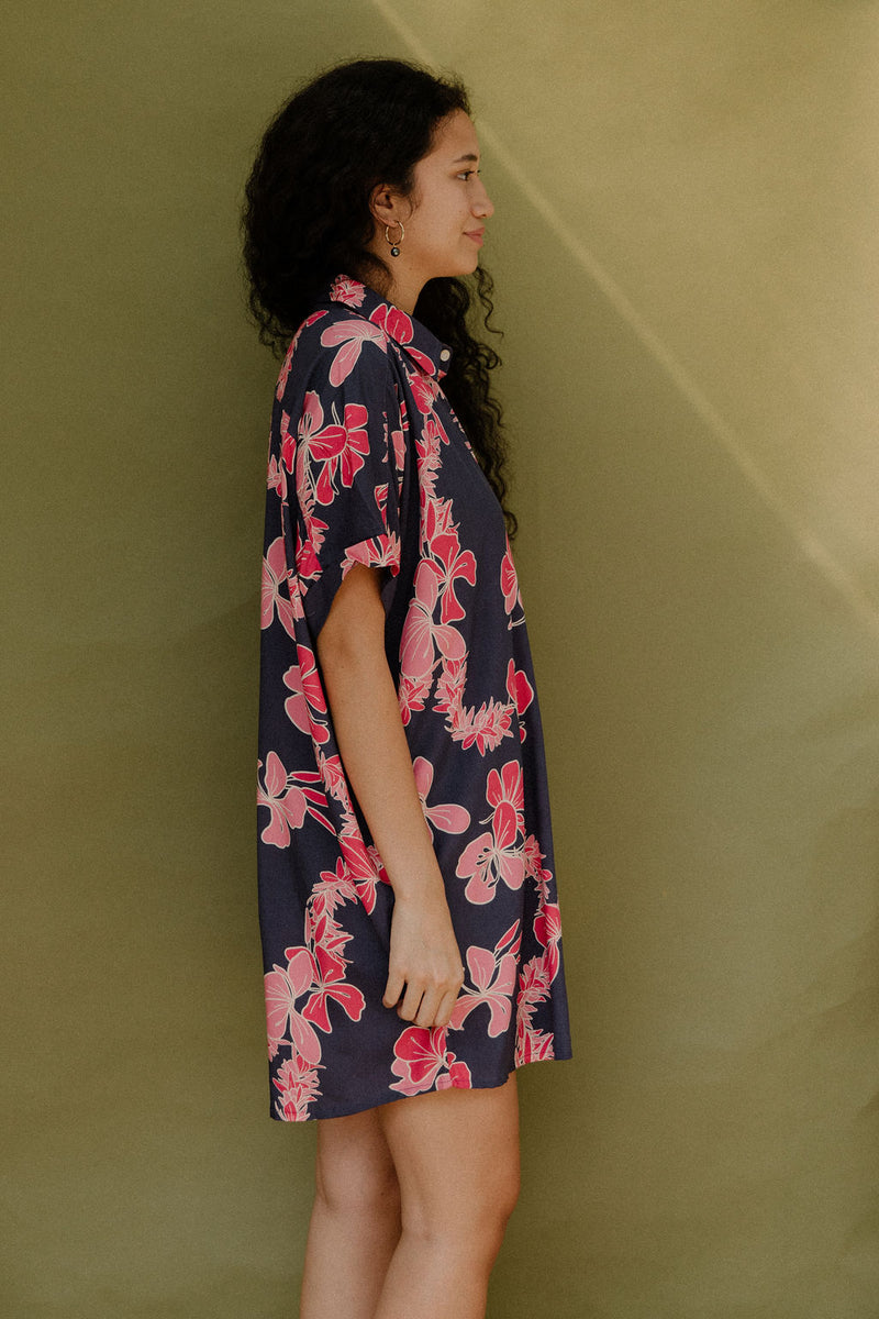 Woman wearing short sleeve shirt dress with pink floral print on dark navy ground.