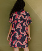 Woman wearing short sleeve shirt dress with pink floral print on dark navy ground.