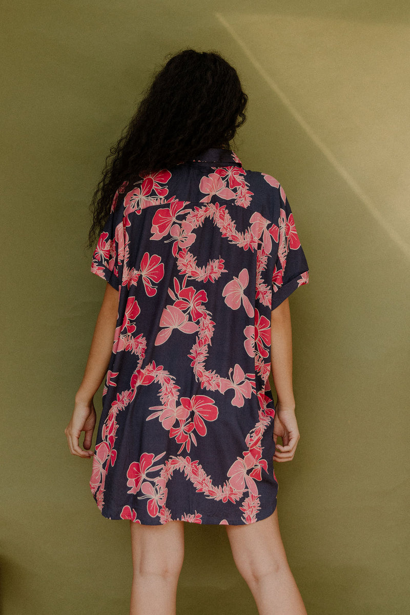 Woman wearing short sleeve shirt dress with pink floral print on dark navy ground.