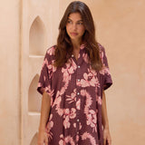 woman with brown hair wearing.a brown/maroon button up dress with pink lei awapuhi print