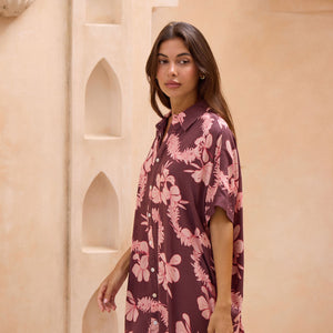 woman with brown hair wearing.a brown/maroon button up dress with pink lei awapuhi print