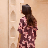 woman with brown hair wearing.a brown/maroon button up dress with pink lei awapuhi print