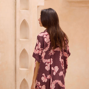 woman with brown hair wearing.a brown/maroon button up dress with pink lei awapuhi print