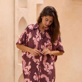 woman with brown hair wearing.a brown/maroon button up dress with pink lei awapuhi print