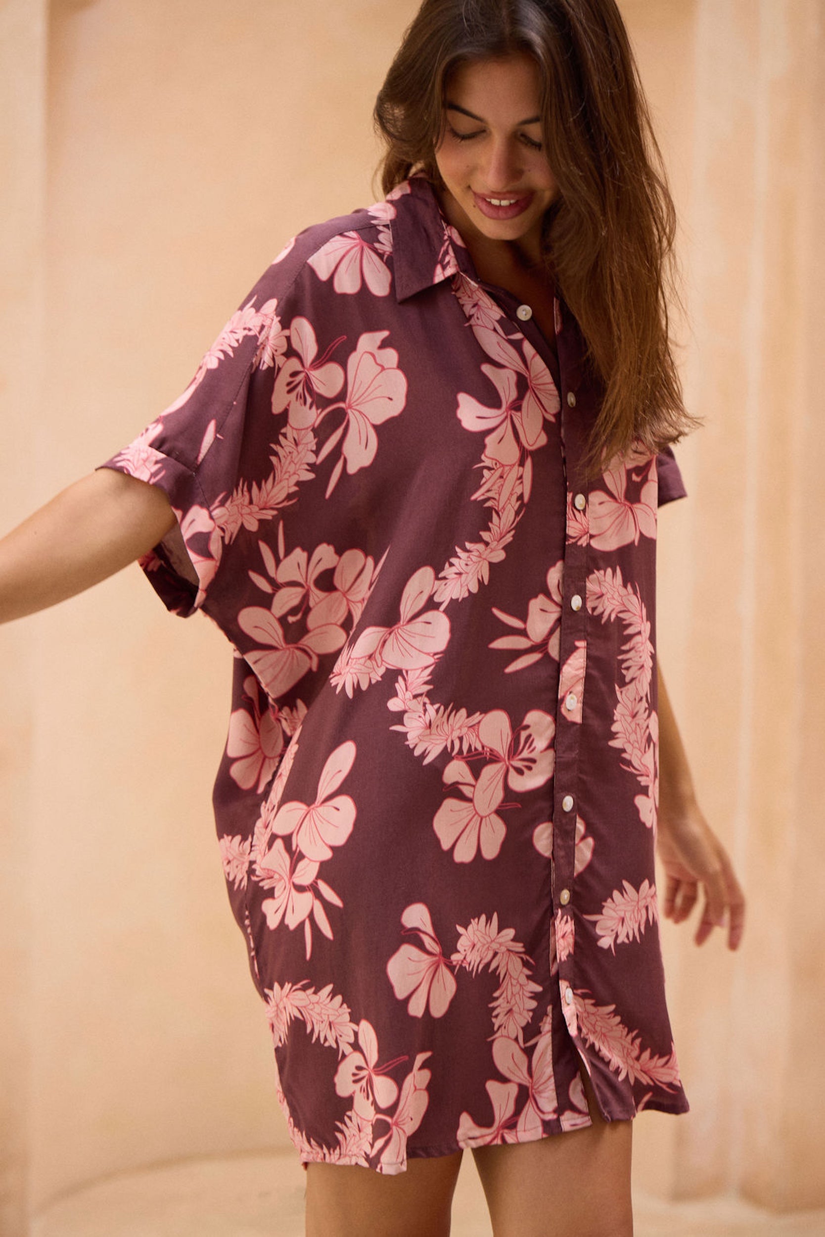 woman with brown hair wearing.a brown/maroon button up dress with pink lei awapuhi print