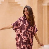 woman with brown hair wearing.a brown/maroon button up dress with pink lei awapuhi print