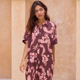 woman with brown hair wearing.a brown/maroon button up dress with pink lei awapuhi print