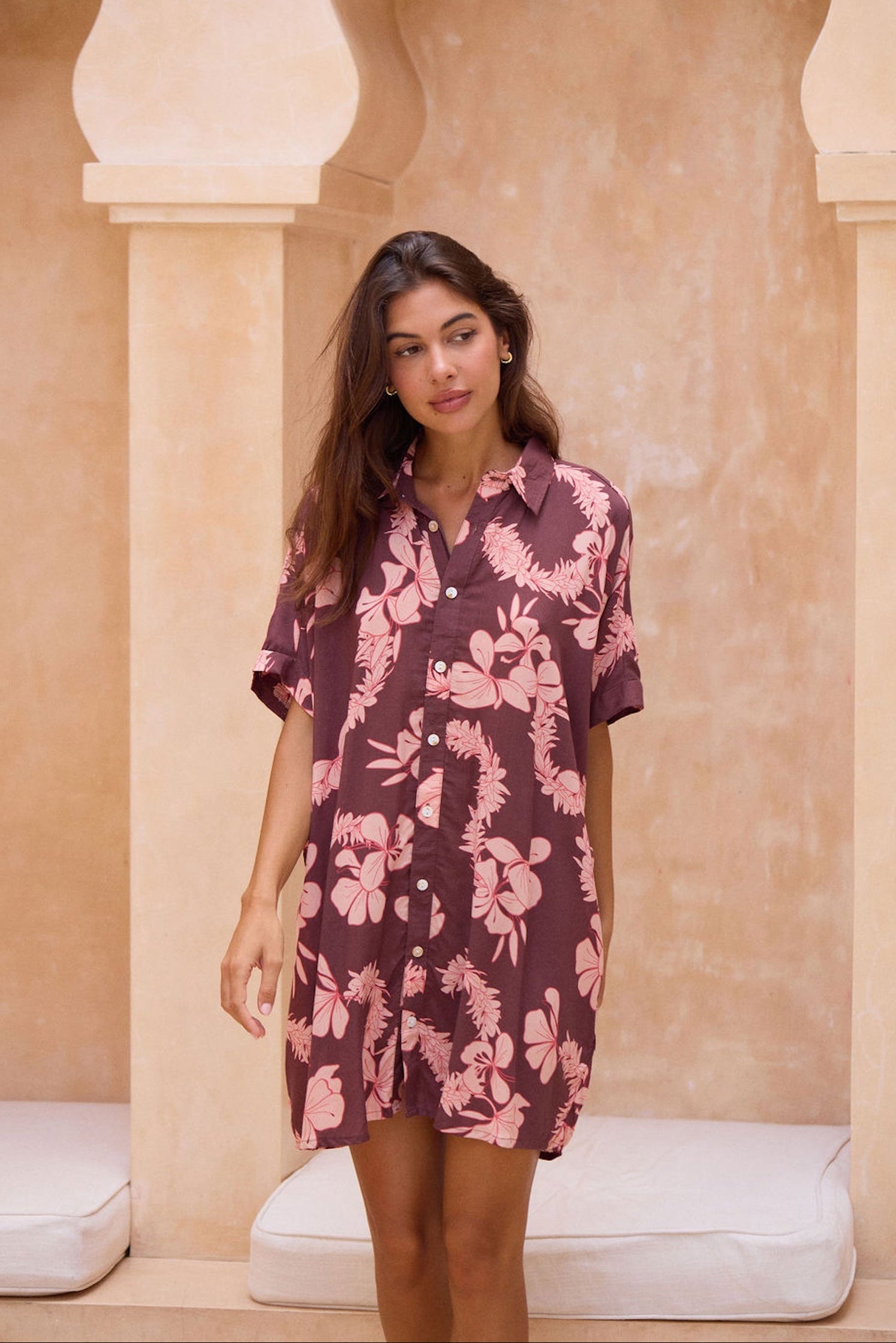 woman with brown hair wearing.a brown/maroon button up dress with pink lei awapuhi print