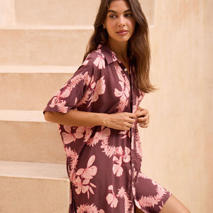woman with brown hair wearing.a brown/maroon button up dress with pink lei awapuhi print