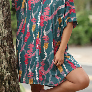 woman with brown hair wearing dark teal button up dress with shell lei print