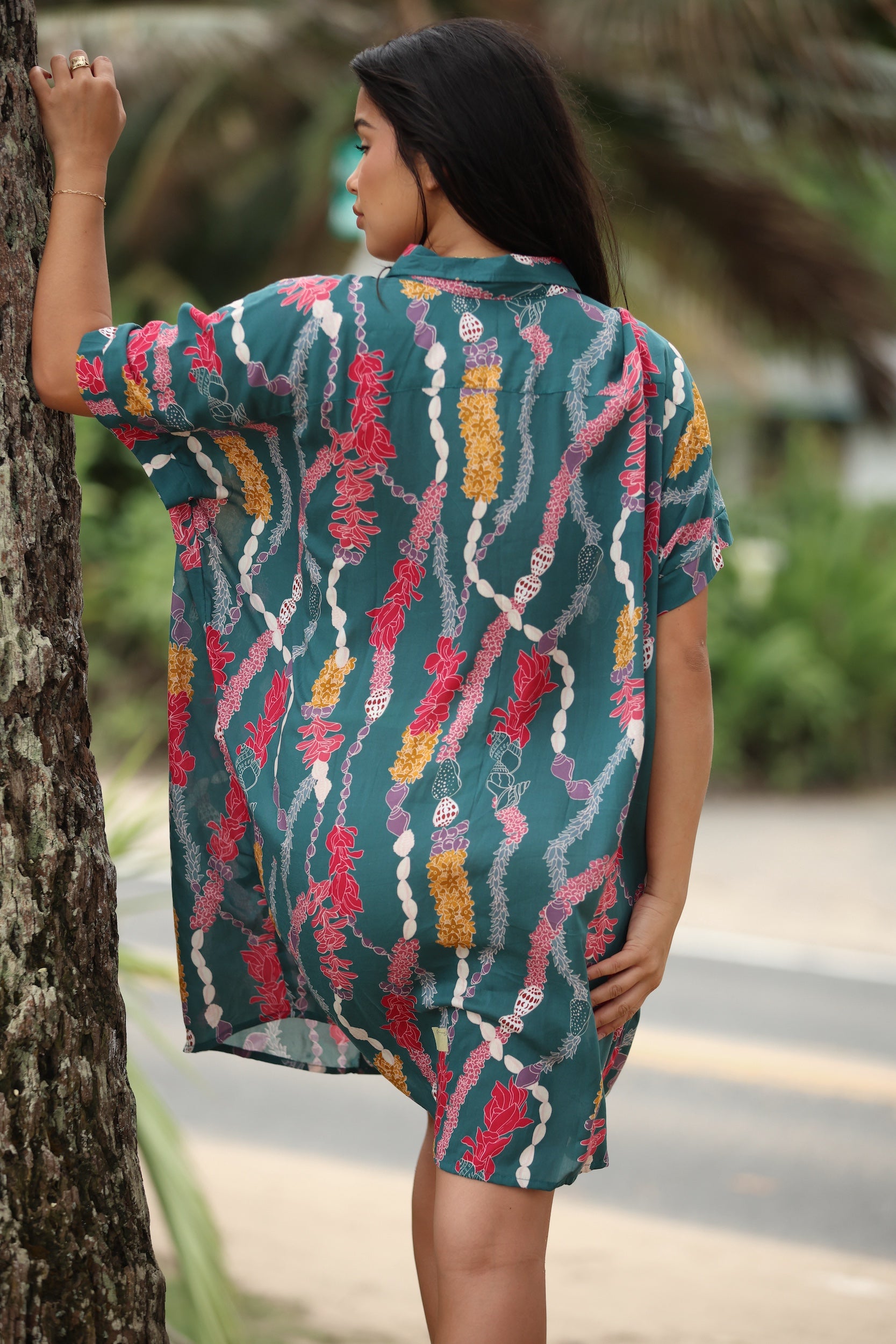 woman with brown hair wearing dark teal button up dress with shell lei print