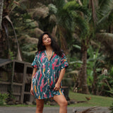woman with brown hair wearing dark teal button up dress with shell lei print