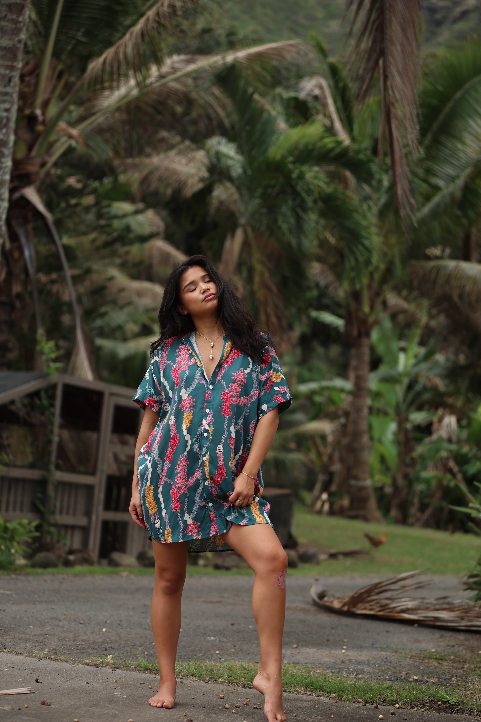 woman with brown hair wearing dark teal button up dress with shell lei print