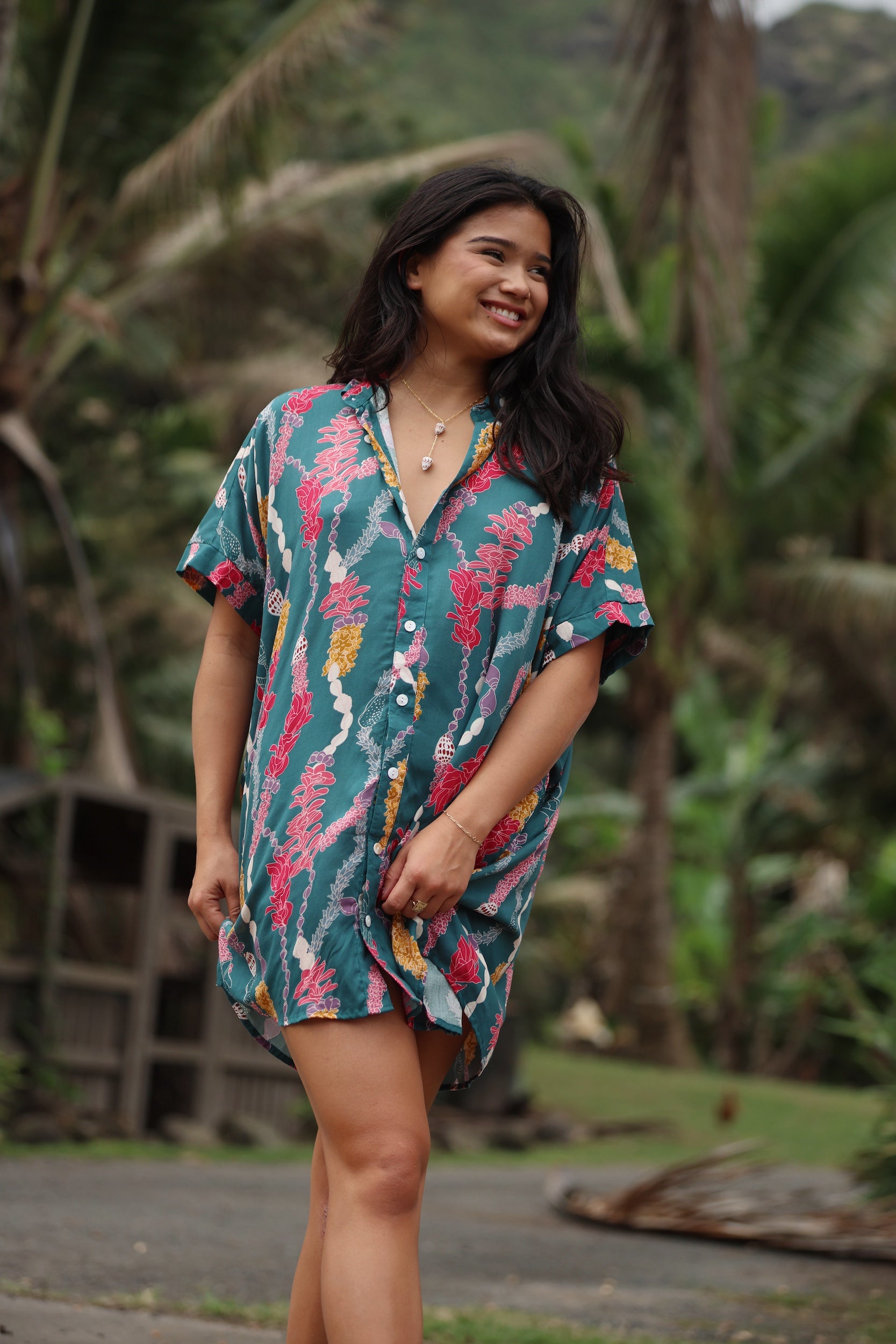 woman with brown hair wearing dark teal button up dress with shell lei print