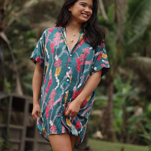woman with brown hair wearing dark teal button up dress with shell lei print