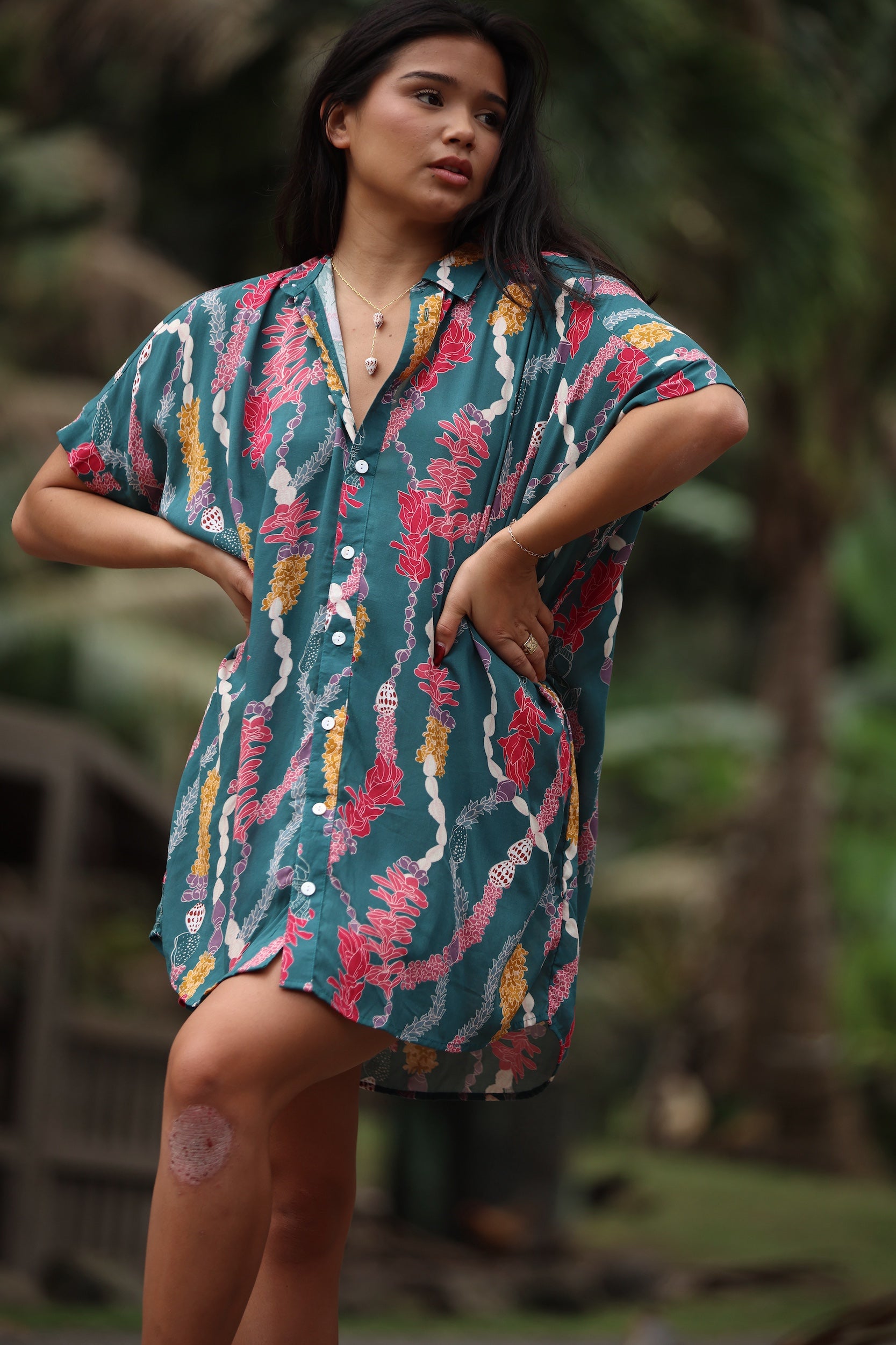 woman with brown hair wearing dark teal button up dress with shell lei print