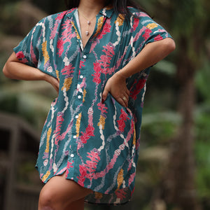 woman with brown hair wearing dark teal button up dress with shell lei print