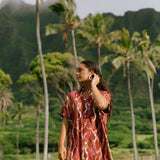 woman with brown hair wearing a red-brown colored button up t-shirt dress with lei print