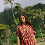 woman with brown hair wearing a red-brown colored button up t-shirt dress with lei print