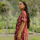 woman with brown hair wearing a red-brown colored button up t-shirt dress with lei print