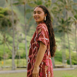 woman with brown hair wearing a red-brown colored button up t-shirt dress with lei print