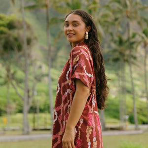 woman with brown hair wearing a red-brown colored button up t-shirt dress with lei print
