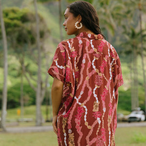 woman with brown hair wearing a red-brown colored button up t-shirt dress with lei print