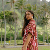 woman with brown hair wearing a red-brown colored button up t-shirt dress with lei print