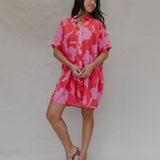 woman with brown hair wearing a red button up collared dress with pink mao flower pattern