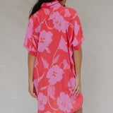 woman with brown hair wearing a red button up collared dress with pink mao flower pattern