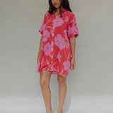 woman with brown hair wearing a red button up collared dress with pink mao flower pattern