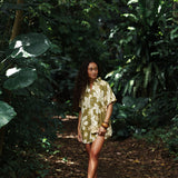 woman with brown hair wearing a button up dress in a green color with naupaka pattern throughout. 