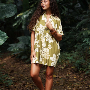 woman with brown hair wearing a button up dress in a green color with naupaka pattern throughout. 