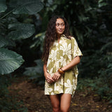woman with brown hair wearing a button up dress in a green color with naupaka pattern throughout. 