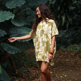 woman with brown hair wearing a button up dress in a green color with naupaka pattern throughout. 