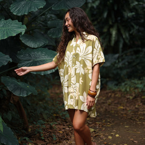woman with brown hair wearing a button up dress in a green color with naupaka pattern throughout. 