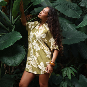 woman with brown hair wearing a button up dress in a green color with naupaka pattern throughout. 