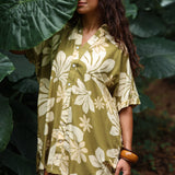 woman with brown hair wearing a button up dress in a green color with naupaka pattern throughout. 