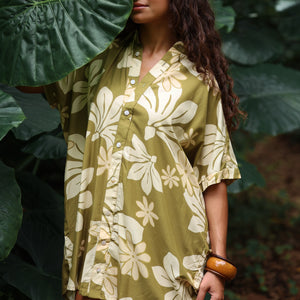 woman with brown hair wearing a button up dress in a green color with naupaka pattern throughout. 
