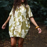 woman with brown hair wearing a button up dress in a green color with naupaka pattern throughout. 