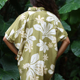 woman with brown hair wearing a button up dress in a green color with naupaka pattern throughout. 