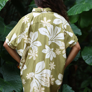 woman with brown hair wearing a button up dress in a green color with naupaka pattern throughout. 