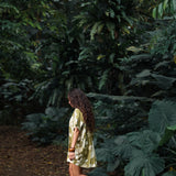 woman with brown hair wearing a button up dress in a green color with naupaka pattern throughout. 
