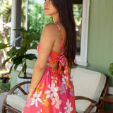 woman with brown hair wearing a pink mini spaghetti strap dress with retro flower print and tie back detail 
